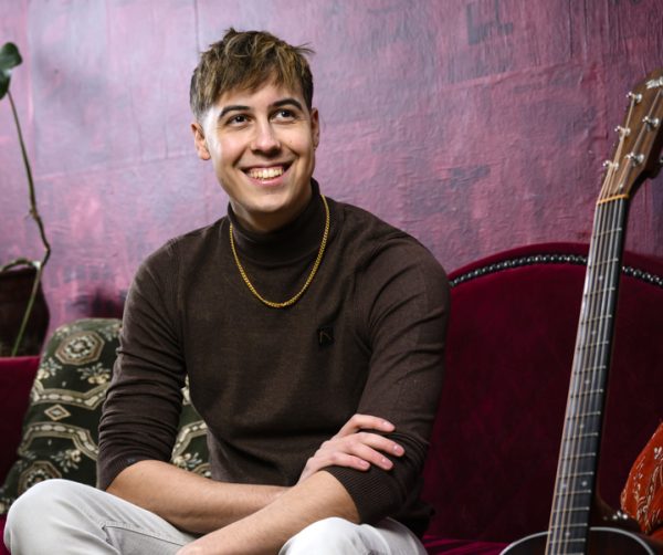 Robin lacht, zittend op bank met gitaar naast hem.