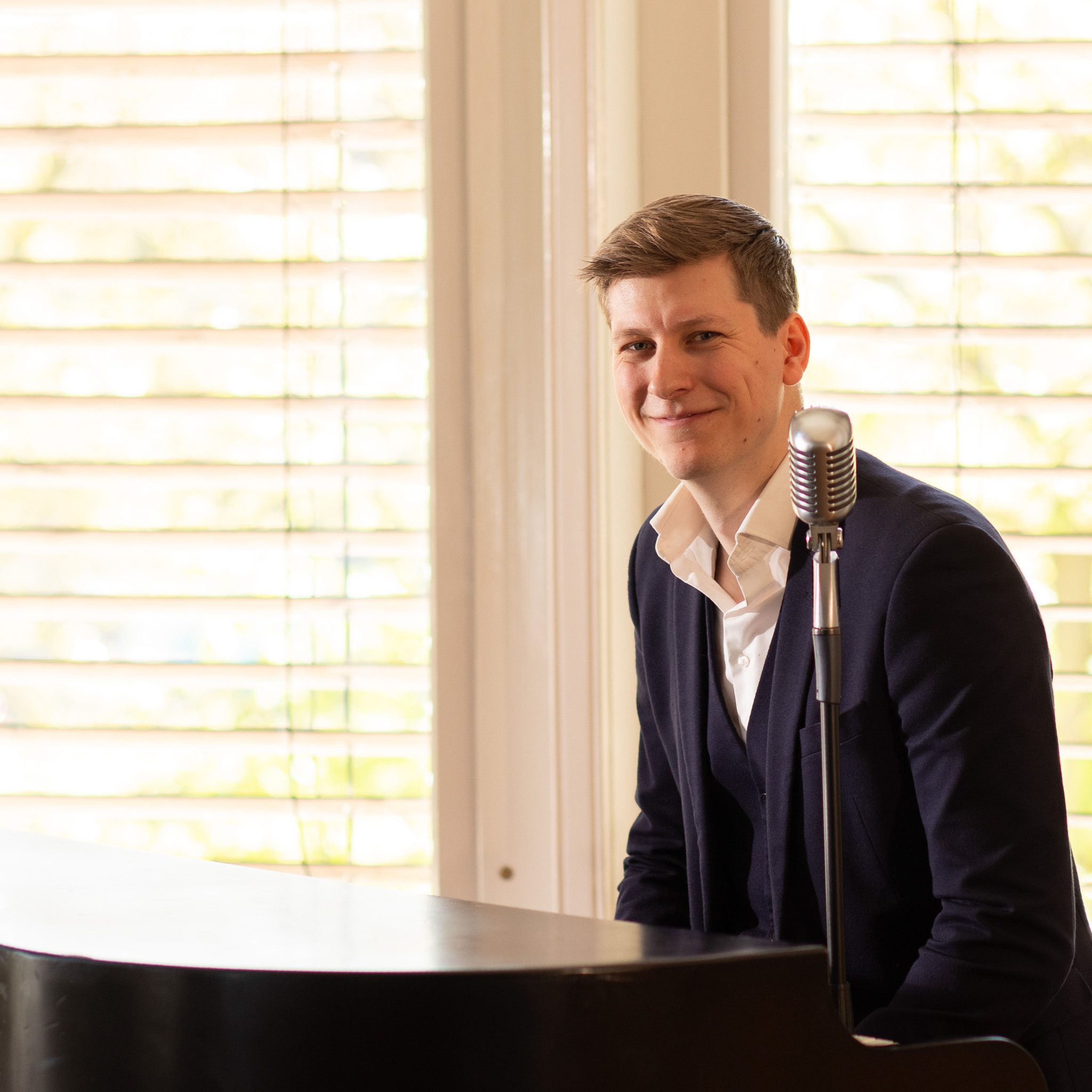 Jorn zit achter de piano en lacht in camera.